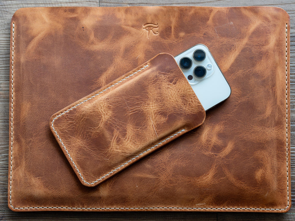 Könnte beinhalten: Ein braunes Leder-Laptop-Etui und Handyhüllen-Set. Das Laptop-Etui hat eine Used-Optik und weiße Nähte an den Kanten. Ein Smartphone ist teilweise in der passenden Handyhülle zu sehen. Das Set dient zum Schutz von Elektronik.