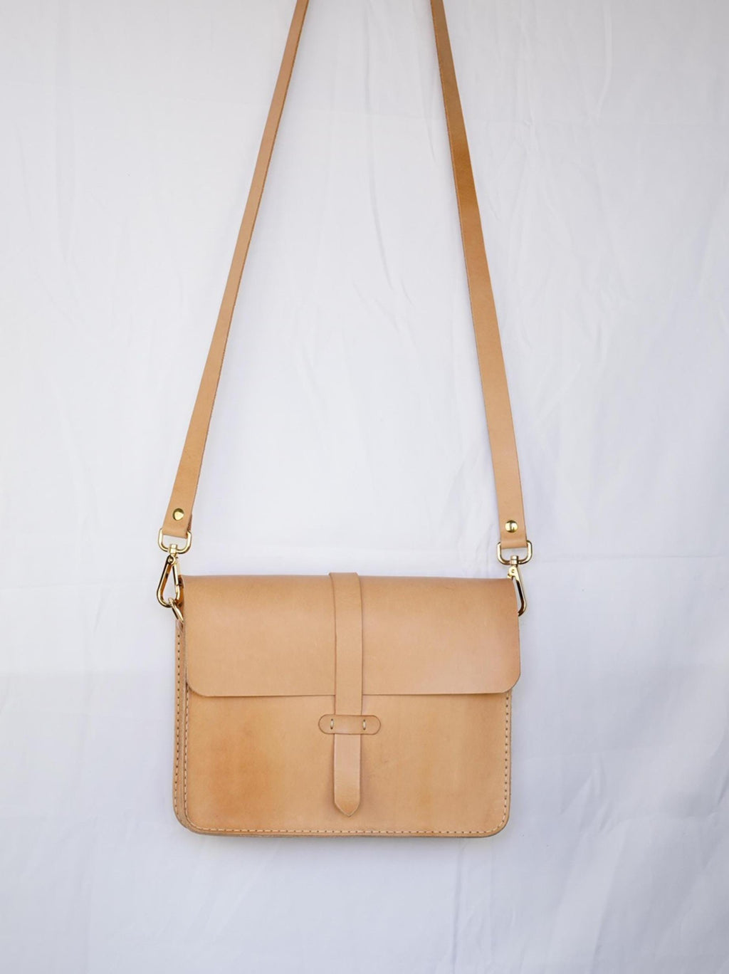 Könnte beinhalten: Eine braune Leder-Umhängetasche mit einer goldenen Schnalle und einem langen Riemen. Die Tasche hat einen Klappverschluss und ein genähtes Design.